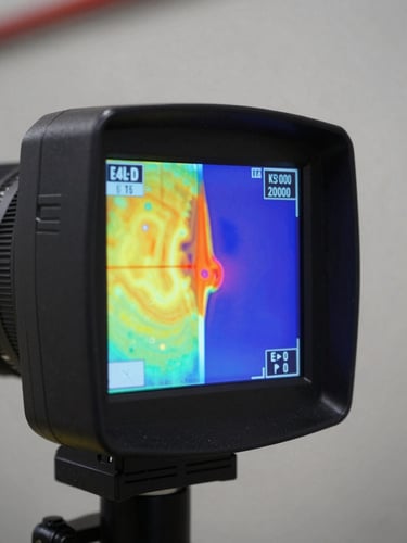 Macro detail shot of a professional thermal imaging camera screen displaying high-contrast temperature spectrum analysis on an industrial wall envelope.