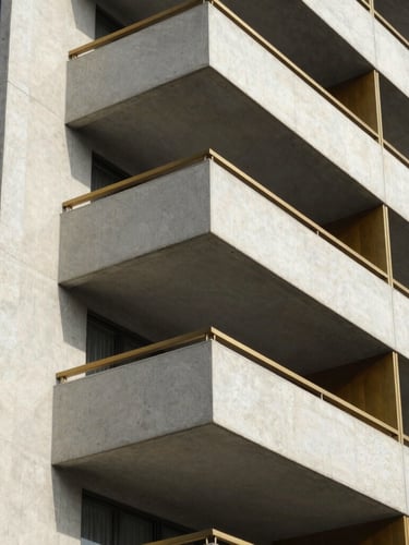 A close-up architectural shot of a modern residential building facade in Borivali, showing clean concrete lines and warm brass balcony accents under bright daylight, 35mm