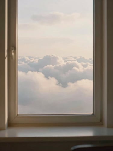 A serene window-seat view of soft white clouds during golden hour, warm light filling the frame, clean minimalist aesthetic, 35mm film style
