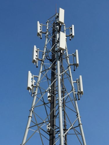 Low-angle heroic shot of a tall telecom transmission tower against a clear blue sky, sharp focus, professional industrial photography