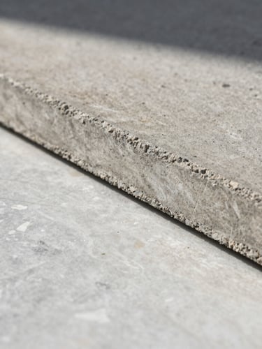 Extreme close-up of raw board-formed concrete meeting a honed travertine slab, natural low-angle morning light casting long soft shadows, emphasizing material texture.