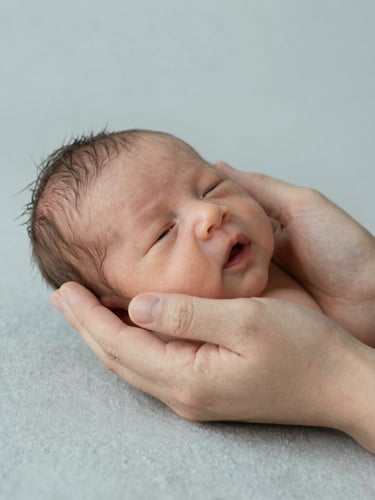 Close-up of hands gently supporting a newborn in soft, diffused daylight, neutral textiles, minimalist editorial photography