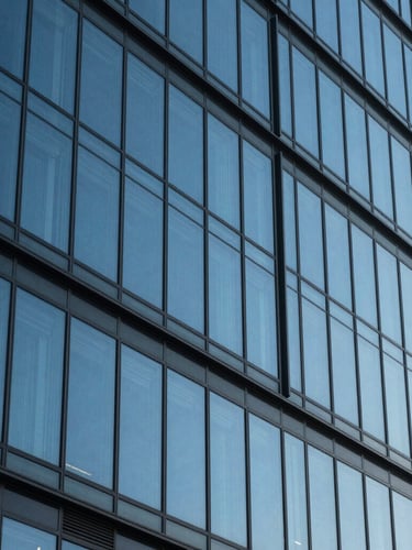 Abstract architectural detail of a modern glass skyscraper facade reflecting a clear blue sky, sharp angles, high contrast lighting, minimalist composition.