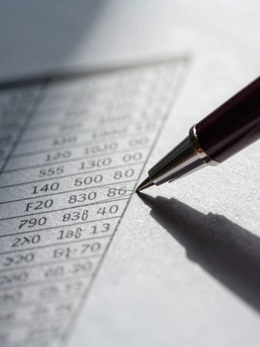 Extreme close-up of a dark pen pointing at a complex amortization table on textured financial paper, sharp architectural shadows, cool daylight.