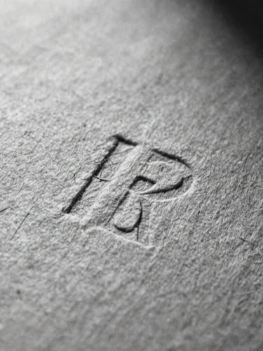 Macro close-up of heavy, textured cotton paper with deep letterpress indentation, stark shadows, high contrast black and white film photography, 35mm grain