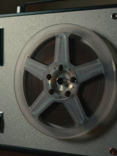 Moody close-up of an old analog tape recorder reel spinning, dramatic side lighting, rich shadows, cinematic look