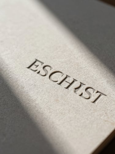Extreme close-up of deeply embossed stationery on heavy neutral stone paper stock, hard directional natural light casting sharp geometric shadows.