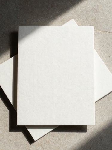 Geometric flat-lay of embossed linen stationery and heavy paper stock on a neutral stone surface, casting sharp, directional shadows.