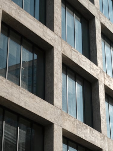 Close-up of architectural concrete and glass facade detail on a commercial building, natural north-facing daylight, geometric shadow lines, no people
