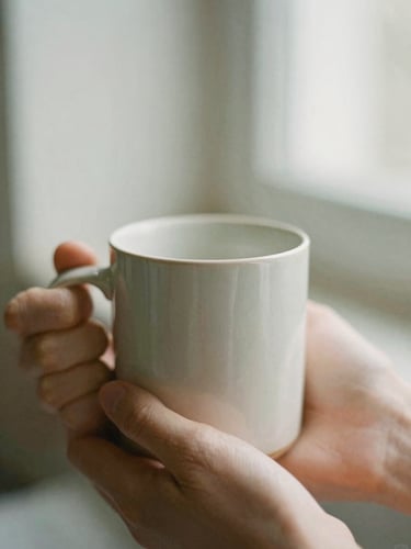 A close-up of a warm ceramic mug held by two hands, soft morning light, muted sage and warm cream tones, shallow depth of field, 35mm film feel