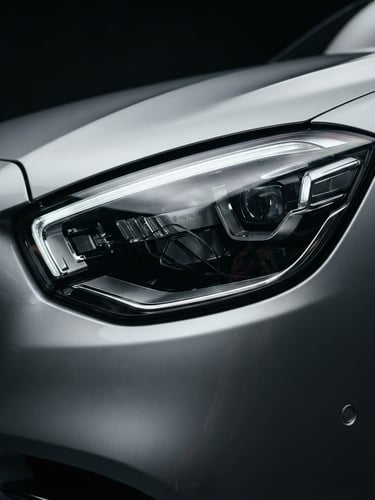 Low-angle heroic close-up of a polished silver luxury sedan headlight, sharp metallic reflections, dramatic low-key studio lighting, 50mm lens, dark background