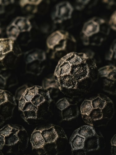 Extreme macro shot of whole, textured ungarbled black peppercorns, moody editorial lighting, deep charcoal and olive tones, 35mm.