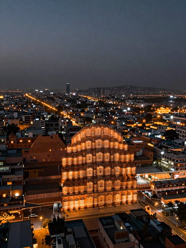 Panoramic overhead night shot of Jaipur city grid — amber streetlights forming a geometric lattice across the frame, left-aligned horizon, wide sky above, no people, city as circuit board not romantic skyline