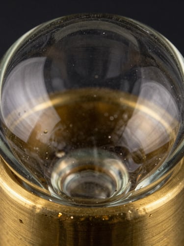Extreme macro crop of hand-poured glass meeting brushed brass, showing realistic texture grain, refraction of light, and subtle material imperfections, dark moody lighting