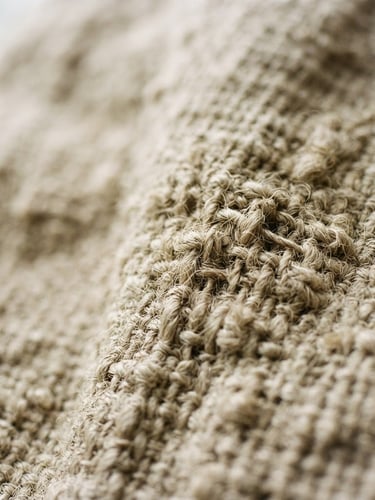 Close-up macro shot of heavy-weight raw Belgian linen with uneven weave structure, soft morning window light, earthy oatmeal tone, shallow depth of field, 35mm