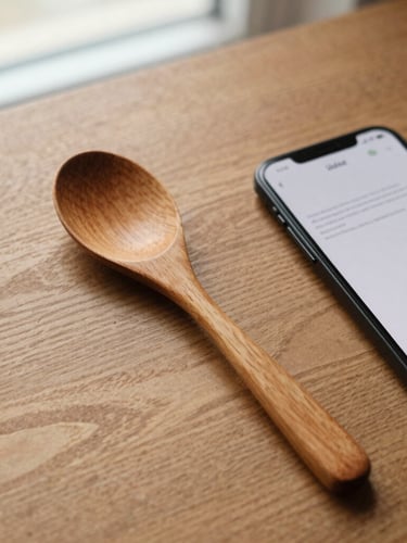 Overhead flatlay of a hand-carved wooden spoon resting on an oak table next to an Android phone showing a minimalist text interface, warm overcast window light, 35mm