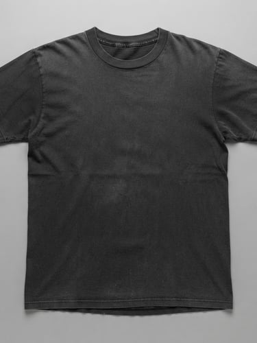 Overhead flat-lay of a perfectly faded 1970s black cotton t-shirt, showing single-stitch hem detail, crisp studio lighting, neutral grey background