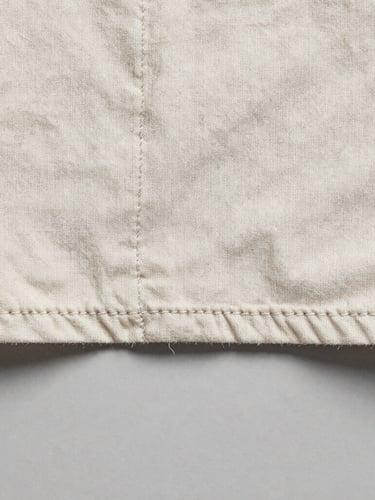 Extreme macro photograph of a single-stitch hem on a heavily faded vintage cotton shirt, showing individual thread fibers, flat studio lighting, neutral grey background
