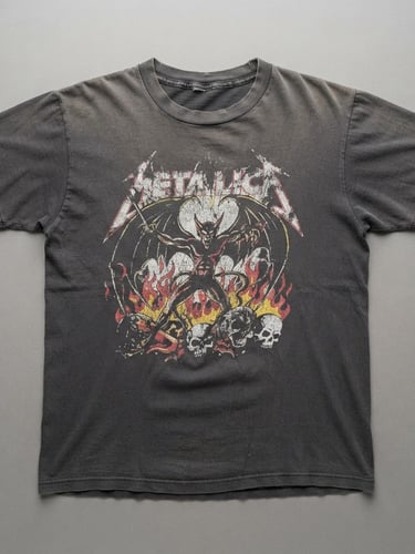 Crisp flat-lay product photography of a naturally faded 1980s black band t-shirt, single-stitch seams visible, flat studio light, neutral grey background, sharp focus