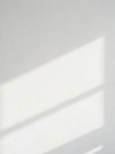 Minimalist high-key photography of soft diffuse white light casting pale architectural shadows on a clean plaster wall, 35mm