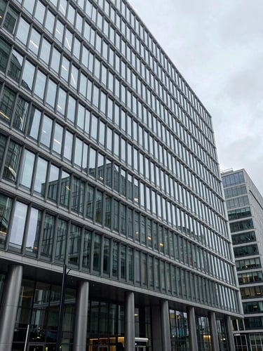 Planos abiertos de escala arquitectónica de un edificio corporativo moderno en la City de Londres, luz de día fría y difusa, estructuras de acero y vidrio templado.