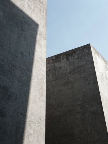 Low-angle heroic shot of monolithic concrete forms under high-contrast daylight with sharp graphic shadows, architectural photography, 35mm