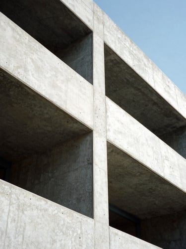 Low-angle heroic shot of raw monolithic concrete forms and sharp steel framing, high-contrast daylight with graphic shadows defining structural form, architectural photography, 35mm