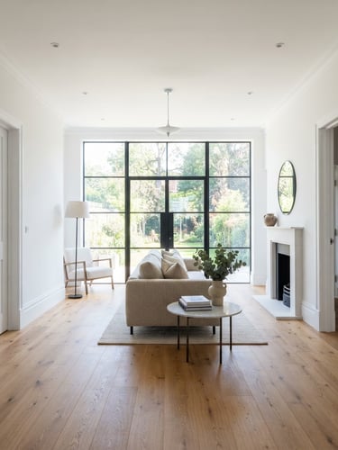 Straight-on bright architectural photography of a freshly completed modern living room with pristine white moldings, clean paint edges, and warm wood floors, flooded with natural daylight through a large window, 35mm lens.