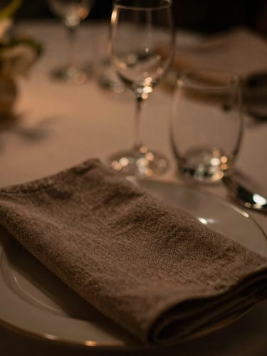 Close-up macro shot of premium textured linen and polished glassware on a corporate hospitality table, warm low-key lighting, shallow depth of field