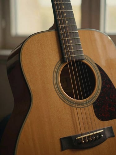 Close-up of a vintage wooden acoustic guitar, worn by time, under soft golden-hour window light, shallow depth of field, rich soft tones, intimate cinematic style, 35mm film.