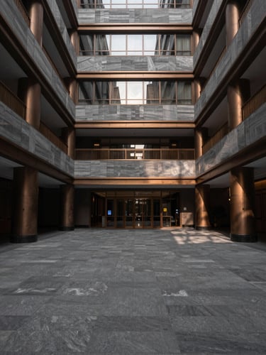 Symmetrical architectural shot of an empty luxury hotel atrium, dramatic morning shadows, desaturated slate and bronze tones, medium format camera