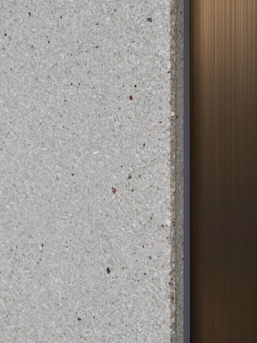 Macro portrait texture of raw split-face travertine stone meeting a brushed bronze profile, sharp architectural shadow, overcast daylight.