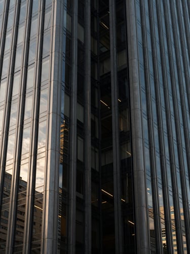 Wide panoramic shot of a modern corporate building facade in São Paulo, sharp glass and steel angles, natural late afternoon side-lighting with deep shadows, high-contrast architectural detail.