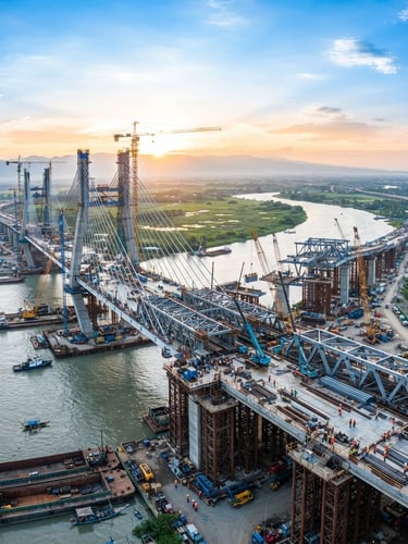 Wide panoramic view of a modern bridge under construction in Central Luzon at sunrise, showing structural steel and active construction, clean professional photography, bright daylight, corporate blue and green tones, sharp focus, wide environmental framing.