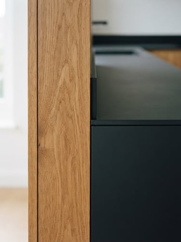 Macro architectural photography of a minimalist kitchen joint, soft natural window light, oak wood grain meeting matte charcoal lacquer, 35mm