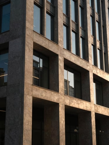 Wide environmental shot of a modern corporate building facade with concrete and glass, dramatic late afternoon light casting long rich shadows, architectural detail.