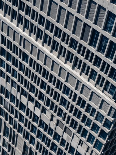 High-angle architectural photography of a modern corporate building facade, sharp daylight, deep blue shadows, concrete gray texture, technical grid overlay, 35mm