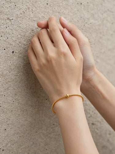 Hands clasping a whisper-thin gold bracelet against a textured stone background, soft diffused lighting, editorial jewelry photography.