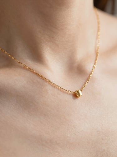 Extreme close-up of a delicate gold chain necklace resting on bare skin, soft diffused natural daylight, warm neutral tones, macro lens, shallow depth of field