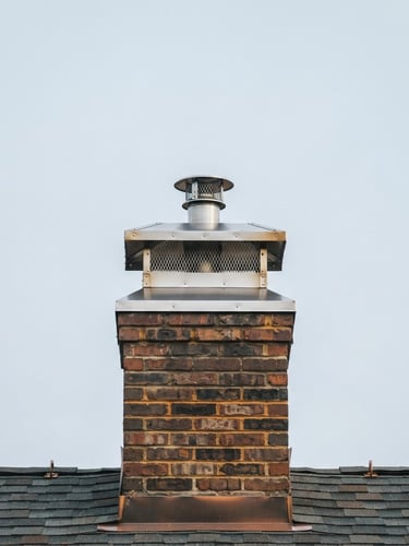 Crisp editorial photograph of a meticulously cleaned chimney cap against a clear New England sky, straight-on architectural framing, natural overcast daylight, rich charcoal and warm amber tones, sharp focus, 35mm lens.