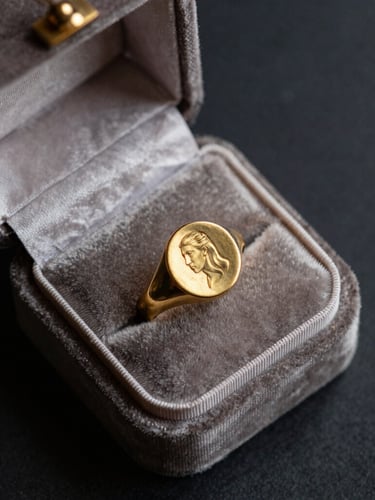 Overhead flat-lay of an open antique velvet jewelry box, a heavy 18k Georgian gold signet ring resting on faded silk, moody directional window side-light, deep charcoal background, rich gold patina