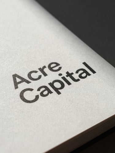 A close-up of a printed brand book for Acre Capital, showing clean typography on heavy textured paper, soft shadows, natural light