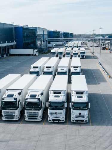 Organized fleet of modern white freight trucks parked in a clean logistics terminal, bright daylight, cool steel blue tones, sharp focus, editorial