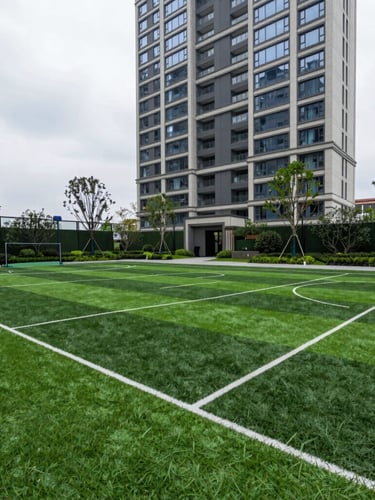 Architectural outdoor photography of a wide-angle synthetic sports court in a luxury condominium, showing sharp lines, dense green turf, and seamless joints under soft overcast daylight.