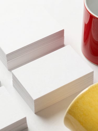 Bright high-key product photography of neatly stacked custom embossed business cards and vibrant sublimated ceramic mugs on a clean white background, macro detail, soft shadows.