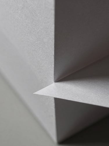 Macro close-up of sharp geometric paper folds, hard directional side-light, crisp paper textures, sharp shadows, neutral monochrome tones, 50mm.