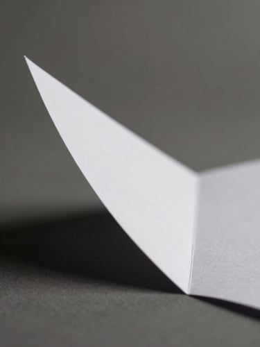 Macro close-up of a sharp folded white paper prototype, hard directional side-light from the left casting deep geometric shadows, minimalist studio photography, neutral monochrome tones, 50mm.