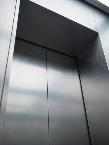 Low-angle architectural shot looking up a modern elevator shaft, sharp metallic reflections, cool crisp lighting, 35mm lens
