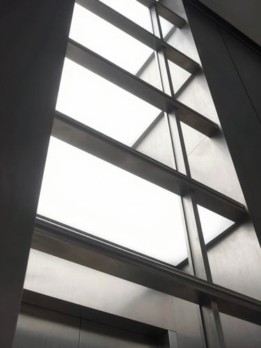 Low-angle looking up a modern illuminated elevator shaft, steel structure, crisp architectural lighting, cool metallic tones, 35mm lens