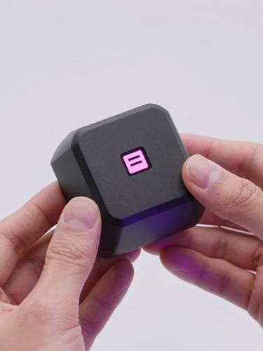 Hands of a designer holding a sleek, matte black 3D printed geometric prototype with integrated NFC chip, soft magenta lighting reflections, minimal studio background
